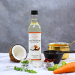 Bottle of Indiyeah cold pressed oil with a coconut, carrot, and other ingredients on a gray background