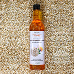 Bottle of Indiyeah cold pressed oil with a label on a background of sesame seeds