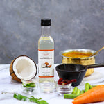 Bottle of Indiyeah cold pressed oil with a coconut, carrots, and other ingredients on a gray background